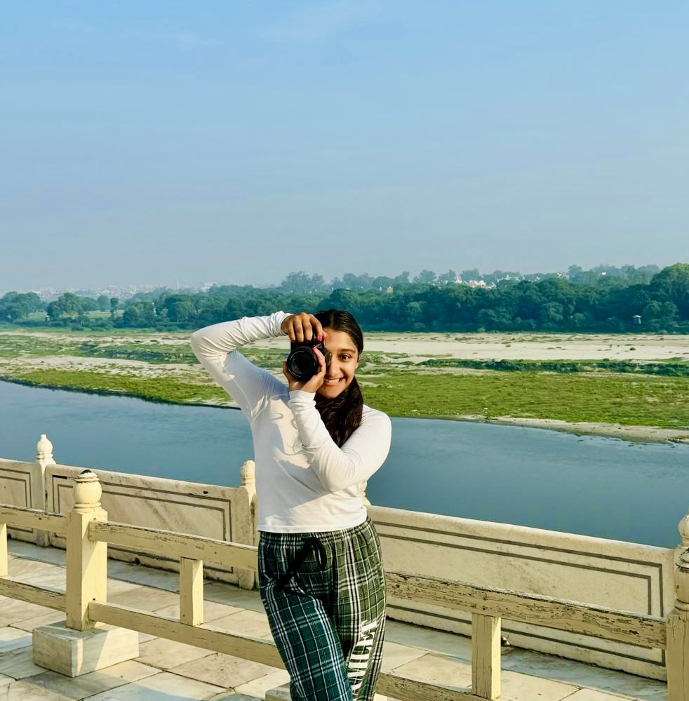 Anoushka Sarathy holding a camera with a river landscape behind her